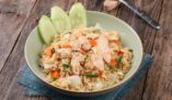 Mouthwatering chicken fried rice with fresh vegetables on rustic wooden table.